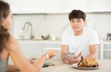 Young guy and young girl drink tea and talk while sitting in kitchen at home