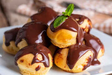 Delicious profiteroles with chocolate and white plate. Selective focus image on light background.