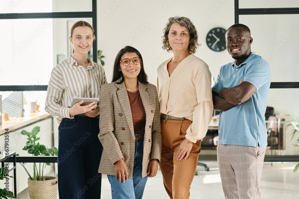 Aufkleber Group of successful intercultural white collar workers in smart casualwear looking at camera with smiles while standing in spacious office