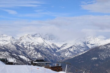 Fototapeta premium Stunning view of Italian mountain range and valley from ski slope in Sauze D'Oulx ski resort, Turin, Italy. Beautiful Italian alpine peaks of snow capped mountains in the Piedmont region.