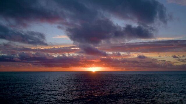Time lapse of sun setting over open sea with moving clouds and waves