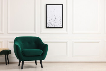 Comfortable armchair and picture on white wall indoors. Space for text