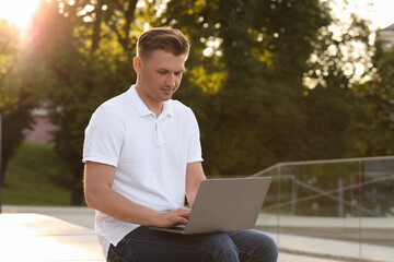 Handsome man using laptop on bench outdoors