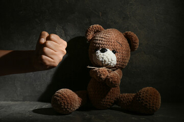 Stop child abuse. Man showing fist to toy bear in dark room, closeup