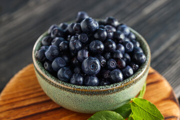 Bowl of tasty fresh bilberries on wooden table, closeup