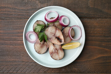 Slices of tasty salted mackerel with onion rings, parsley and lemon wedge on wooden table, top view