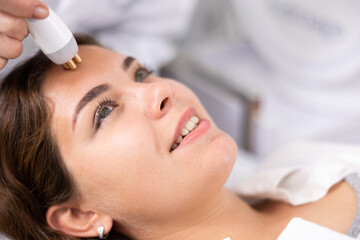 Close-up view of face of delighted young woman undergoing radio frequency lifting procedure