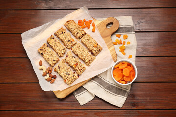 Tasty granola bars, dried apricots and nuts on wooden table, flat lay