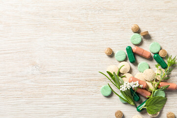 Different pills and herbs on wooden table, flat lay with space for text. Dietary supplements