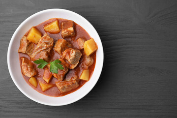 Delicious goulash in bowl on black wooden table, top view. Space for text