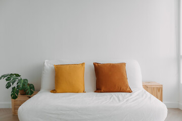 Simple minimal sofa decorated with brown yellow pillows in white living room.