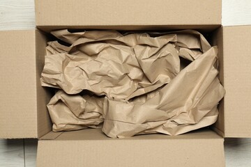 One open cardboard box with crumpled paper on white wooden floor, top view