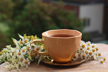 Cup of delicious chamomile tea and fresh flowers outdoors