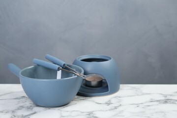 Fondue set on white marble table against light gray wall, space for text