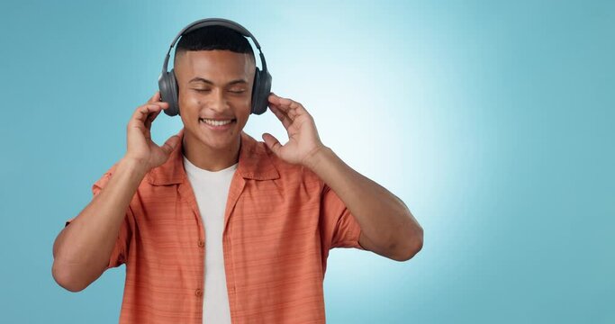 Headphones, dancing and young man in a studio listening to music, playlist or album for entertainment. Happy, smile and male model from Mexico streaming or radio with technology by blue background.