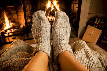 Legs of a woman wearing two socks comfortably in front of the fire on a winter night.
