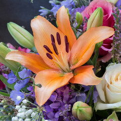 Macro texture background of fresh bright flowers in an indoor florist arrangement, featuring an orange lily and a lavender rose