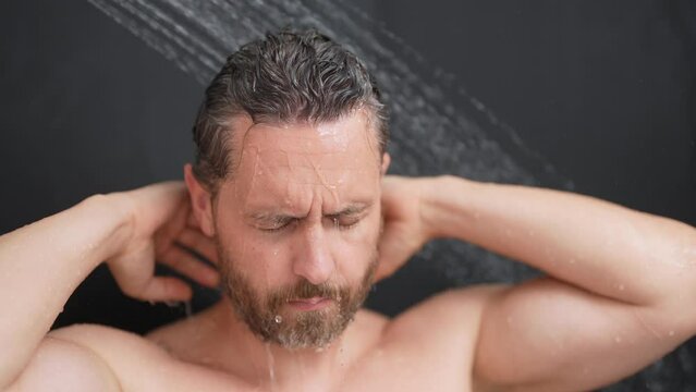 Sexy man washing hair in bathroom. Guy bathing shower head in bathtub. Male face in shower. Man taking shower in bathroom. Guy showering. Bathroom concept. Man is under water drops in bathroom.