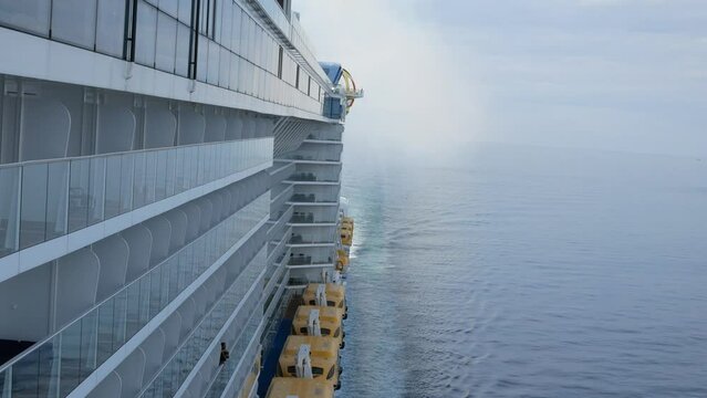view to the back aft of the cruise ship from front deck area with side view of the passenger cruise ship while cruising in the sea in day time with many lifeboats