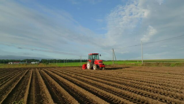 Slow rotation around bright red tractor in plowed field in morning light