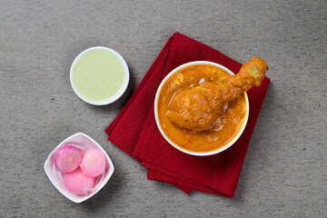 Top view of butter chicken in bowl with onion and chutney
