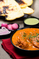 Closeup of butter chicken with naan and chutney