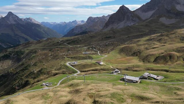 A stunning aerial view of Warth, Vorarlberg in Austria, showcasing the majestic mountain Alps, scattered residential housing, and a light blue sky with wispy clouds on the horizon