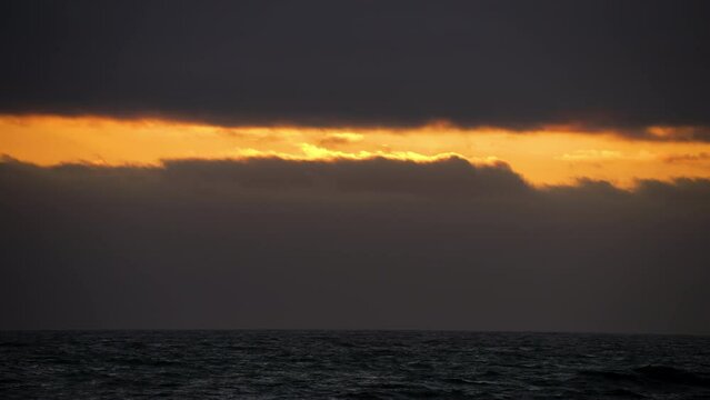 Golden sunset light through dark stormy clouds over the ocean