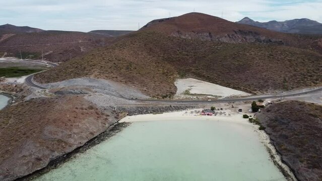 Aerial panning shot over Playa El Tecolote near La paz Baja California Sur Mexico with view of the dried up landscape, the calm sea and a beach and the mountains in the background