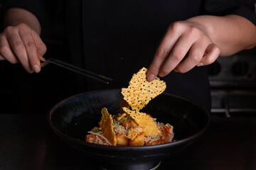 A chef's hands are seen garnishing a plat of modern Japanese food.
