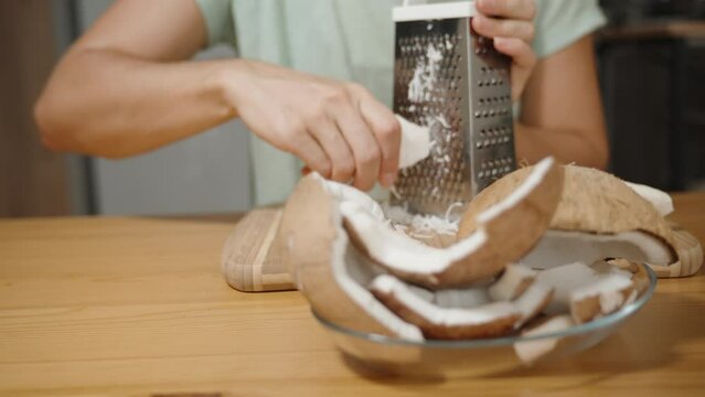 A plate with coconut pieces, and the focus shifts to the background, showing a woman grating it into shreds on a metal grater.