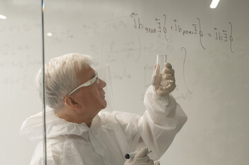 An elderly Caucasian male chemist in a protective suit writes on glass. 