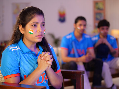 Cricket fans watching a live match at home - Praying for the victory of Indian cricket team  female cricket fan. Siblings engrossed in watching a live cricket match on a large-screen television - w...