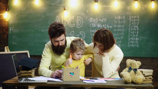 Schoolboy and parents studying. Parents teaching children. Family in early development concept. Father mother and child son painting together at home.