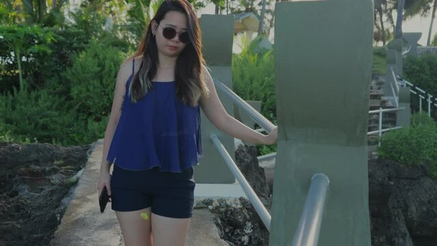 Front view of a girl walking at Taga beach while holding the hand railing during a bright morning, slow motion