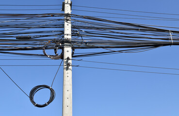 messy electrical cables wiring on concrete electric pole with clear blue sky background, roadside...