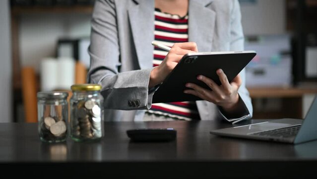 Businesswoman hands working with finances about cost and calculator and laptop with tablet, smartphone at office in morning light.