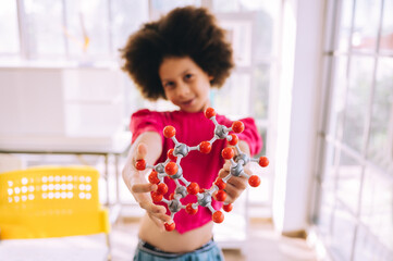 Little girl having fun holding a molecular model learning chemistry science in the classroom....