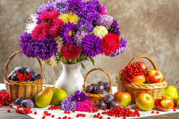 Autumn still life. A vase with asters, baskets of fruit, apples and plums