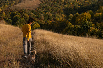 Young woman with a dog hiking through autumn fields and hills against blue sky during warm day. Weekend, leisure, sport