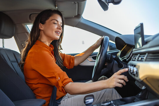 Happy business woman listening to music while traveling with her car around the city. Woman turning on car air conditioning system, car air conditioner on off button