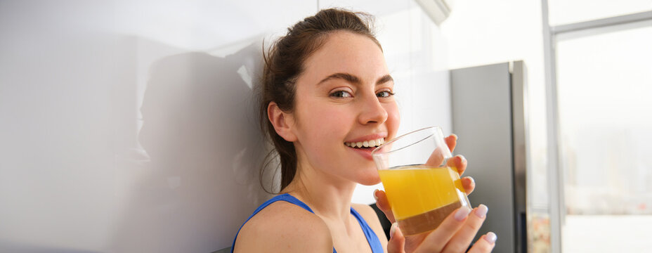 Portrait of smiling brunette sportswoman, drinking fresh juice, detox drink, enjoys freshly squeezed beverage after workout training session