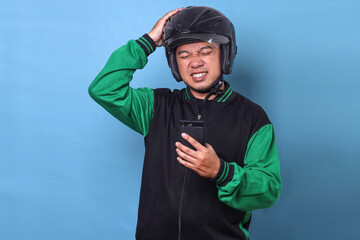 Adult Asian man work as commercial online taxi driver holding smartphone suffering from headache or...