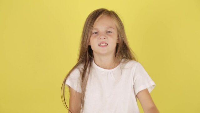 Portrait of angry sad little kid girl, posing isolated on yellow color background in studio. Children's emotions concept