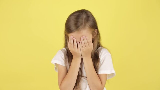 Kids problems. Studio portrait of upset child girl crying and wiping her tears, yellow background.