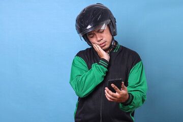 Adult Asian online taxi driver wear helmet, gesturing sad expression  looking at smartphone, not getting order from customer