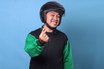 Carefree online motorcycle taxi driver in helmet looking at camera smiling while showing love heart symbol with fingers