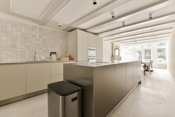 a modern kitchen with white tiles on the walls and floor, along with a black trash can in the corner