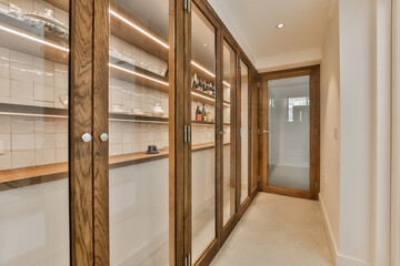 a long narrow hallway with wooden cabinets and white tiles on the walls, along with glass doors leading to another room