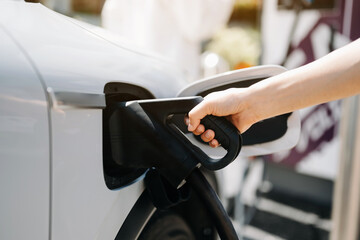 Obraz premium Hand plugging in a charger in an electric car socket.Electric car or ev is charging at station..